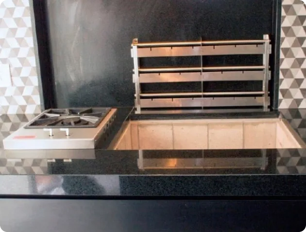Cooktop embutido na bancada ao lado da churrasqueira, com suporte ao fundo